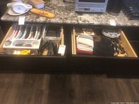 Two kitchen drawers with various utensils organized in a white plastic cutlery tray and loose in the drawer, and kitchen linens folded in the second drawer.