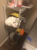 White metal laundry rack with cleaning supplies, towels and accessories in utility room corner.