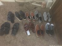 All 7 pairs of men's footwear arranged on carpet, showing various types including slides, slip-ons, boots, sandals, and sneakers.