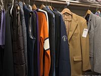 Full view of men's tops including sweaters, vests, and sports coats hanging on hangers in a closet.