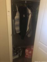 Closet view with jackets hanging and shoes on the floor along with a red bag.