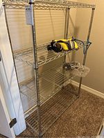 Full view of the 4-tier metal wire shelving unit with items on second and third shelves. Shelving unit stands on carpeted floor within a room.