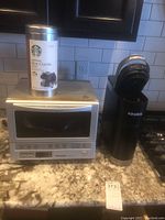 Panasonic toaster oven and Keurig coffee maker on kitchen countertop with Starbucks Hot Cocoa tin on top of oven.