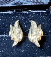 Front view of pair of yellow gold earrings on black background showing curved design and diamond accents