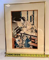 Framed antique Japanese Ukiyo-e woodblock print featuring two figures in traditional dress, with tape measure showing approximate width of frame.