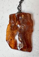Close-up front view of the amber pendant showing natural ridges, translucent brown amber with inclusions, mounted on metal chain.