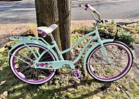 Full side view of the beach cruiser bicycle on grass with a tree in background showing turquoise frame and purple tires with white sidewalls.