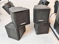 Six Bose small cube mini speakers with attached black metal mounting brackets, front view showing Bose logo on grilles.
