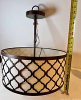 Side view of round metal ceiling light fixture with lattice design and measuring tape showing height about 15 inches.