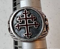 Close-up front view of ring showing red enamel Cross of Lorraine symbol with clover-shaped ends on a dark oxidized round face.