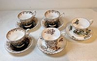 All five Royal Albert cups and matching saucers with distinct floral patterns and gold trim displayed on table.