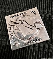 Close-up front image of the square silver brooch showing the Toronto Blue Jays bird head with maple leaf and baseball, along with engraved text 'World Series 1992 Baseball Champions' and artist signature.