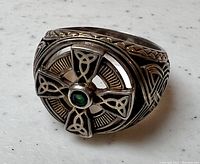 Close-up of the ring front showing detailed Celtic cross with green stone center and intricate silver knotwork surrounding the cross.