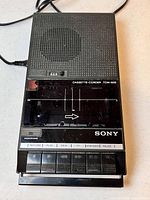 Full frontal view of the Sony TCM-828 cassette-corder showing speaker grill, cassette compartment, control buttons, and power cord.