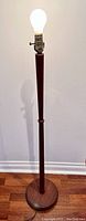 Full view of the vintage floor lamp illuminated, showing tall tapered teak wood pole and round base.
