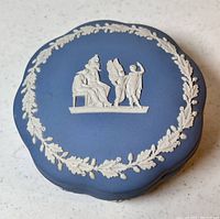Top view of the Wedgwood blue trinket box showing classical white relief decoration of seated and winged figures and wreath border.