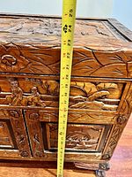 Close-up showing carved floral motifs on the cupboard top with measuring tape indicating a height around 24 inches