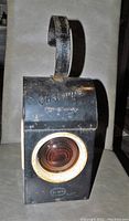 Front view of black Chalwyn lantern showing embossed marking and amber lens with rusted metal frame.