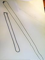 Two silver chains laid flat, the longer chain thin and the shorter chain thicker in appearance.