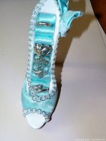 Photo showing five silver rings arranged inside a miniature blue high heel shoe ring holder made from fabric with silver trim and bow detail.