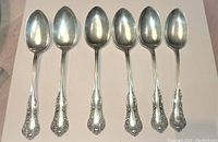 Front view of all six matched sterling silver tablespoons displaying ornate handle designs and polished bowls.