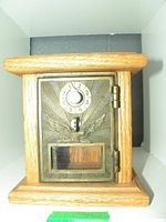 Front of the bank replica showing wooden box with metal door featuring combination dial, eagle emblem, coin slot, and viewing window.