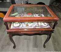 Full view of the vintage wooden and glass display case containing assorted costume jewelry, showing the structure and contents inside.