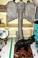 Front view of large wooden elephant head wall decoration with black leather elephant and small elephant figurines in foreground on wooden base.