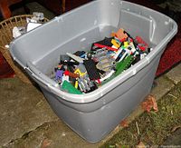 Large gray plastic tote partially filled with assorted LEGO bricks, plates, wheels, and specialty pieces visible on top