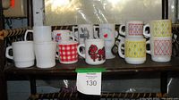 Shelf containing 11 assorted milk glass mugs including patterned, advertising, and plain styles