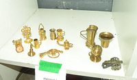 Lot of mostly brass miniature decorative items including vessels, musical instrument, scale, candlestick, and a miniature metal cannon.