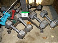 Photo showing multiple hexagonal metal dumbbells in various weights including 5 lb and 8 lb, some smaller colored neoprene weights in background.
