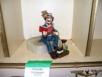 Ron Lee 1985 Hobo Clown figurine sitting on a gray base, holding a red Sales Manual book and a walking stick, detailed with a clock and shoe box on the base.