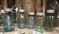Seven vintage mason glass jars arranged side by side with metal lids, some with blue tint, others clear
