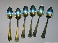 Six sterling silver sugar spoons arranged in a row showing front side with polished finish and design details.