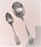 Two silver spoons on white background, serving spoon is large with scalloped shell bowl and ornate handle, tea spoon is smaller with plain handle.