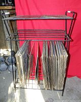 Full front view of the black metal wire record stand showing lower rack filled with vinyl records and an upper shelf.