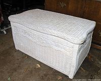 Side angle showing white wicker trunk box with woven sides and lid, decorative carved panels visible