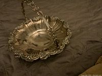 Front angled view of the silverplate footed basket with handle showing detailed ornate design and scalloped edges.
