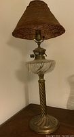 Full view of the electrified oil banquet lamp showing the brass base and glass reservoir with swirled design, plus the optional woven brown conical lampshade.