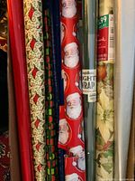Multiple rolls of Christmas wrapping paper showing Santa Claus, stockings, and poinsettia patterns packed together in a box.