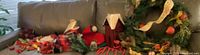 Photo showing various Christmas decorations arranged on a couch including ribbons, floral picks, a house-shaped Advent calendar, candles, and a Christmas wreath.