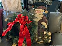 Photo shows the green Christmas wreath adorned with pinecones and a large red velvet bow next to the black metal sleigh decoration with Santa Claus and Christmas trees.