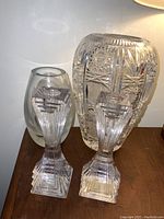 Photo showing two Mikasa crystal candlesticks in front of a large cut Krosno Poland crystal vase and a medium frosted etched floral Krosno Poland vase on a wooden surface.