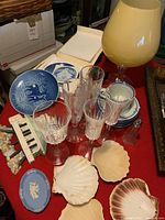 Top view of the lot showing B&G and Wedgwood porcelain plates, crystal wine flutes, Mikasa cup and saucers, shell-shaped baking dishes, Murano style large yellowish glass lamp or vase, and salt and pepper shakers.
