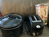 Photo showing Rival black crockpot slow cooker with glass lid beside black 2-slice toaster and boxed Braun Multipractic handheld blender