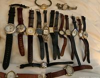 Wide view of 14 assorted wristwatches laid out on a white surface, showing various strap materials, dial shapes and colors.