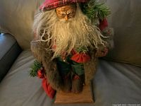 Front view of the Jena Hall Santa figurine dressed in fur and colorful clothing sitting on a brown wooden base.