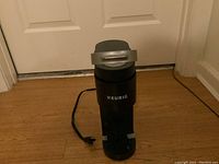Front view of black Keurig coffee maker with Keurig logo and power cord visible on floor