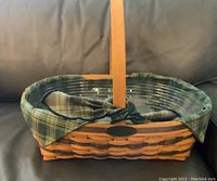 Rectangular woven wood basket with green plaid fabric liner and matching bow tied on handle.
